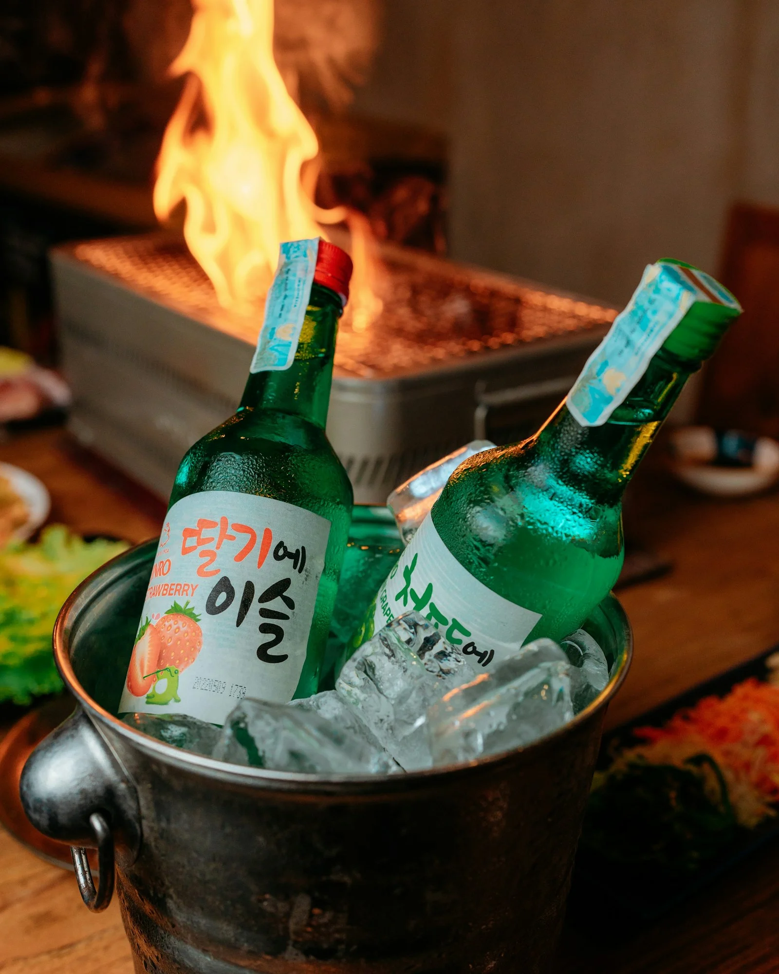 Soju bottles chilling in ice beside a Korean BBQ grill